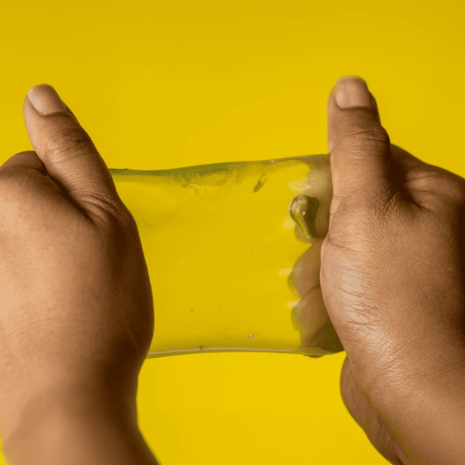 A pair of hands stretching a translucent yellow jelly cube sensory toy against a bright yellow background.