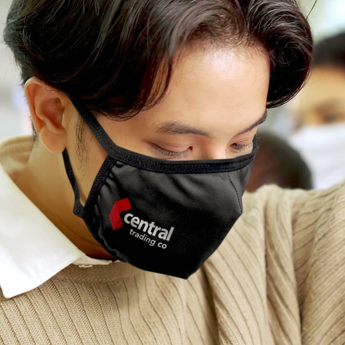 A black reusable cotton face mask with a logo, worn by a person.