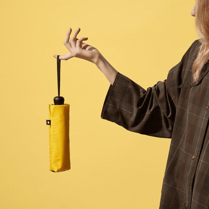 A yellow compact umbrella held by a person, with a plain background and a visible logo on the umbrella.