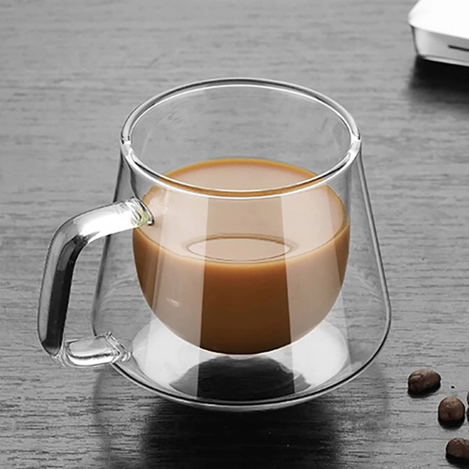 A transparent glass coffee cup with a unique design, featuring a brown beverage inside and a handle.