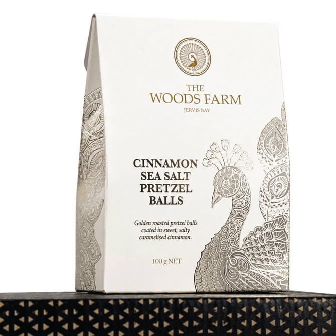 A bag of 100g cinnamon sea salt pretzel balls in a white and gold design, featuring a peacock motif.