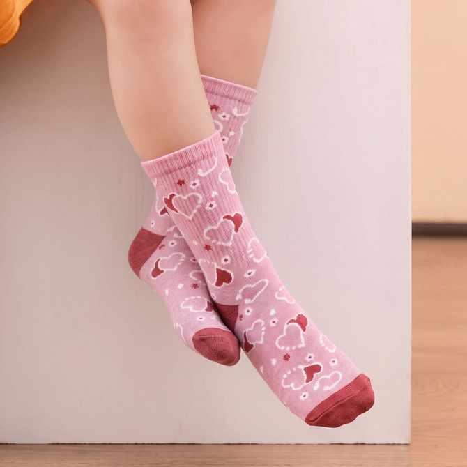 A pair of pink knitted kids' socks featuring heart patterns and a reddish band at the top, resting on a white surface.