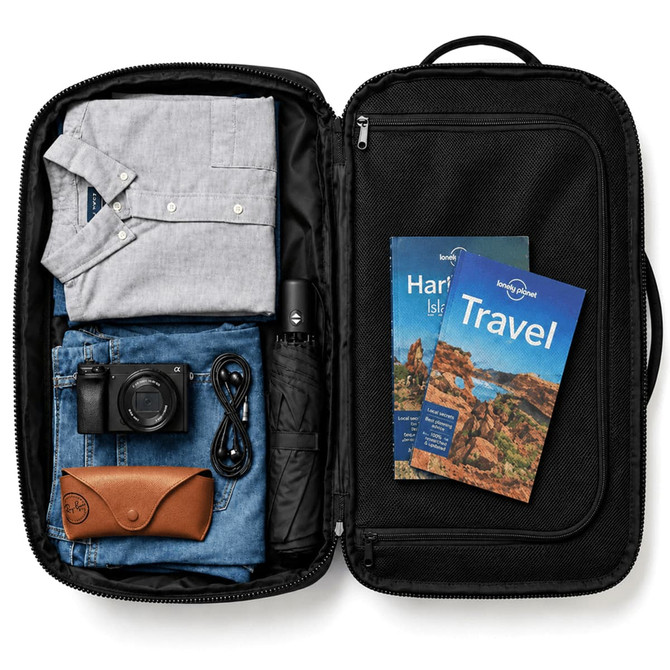 A black backpack opened to reveal a grey shirt, blue jeans, a camera, an umbrella, and travel guides.