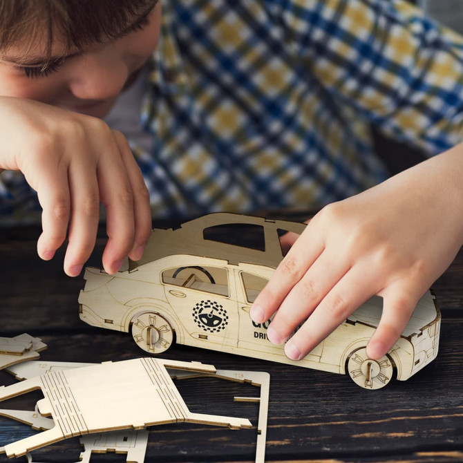 A wooden model of a sedan car, featuring natural wood tones, with a child assembling it on a wooden surface.