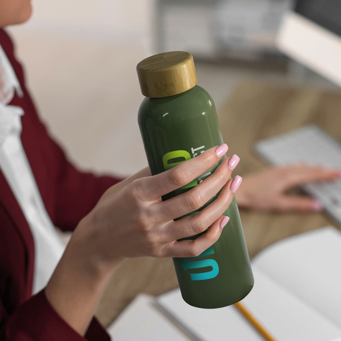 A drink bottle in olive green with a bamboo lid, held by a person, features a logo on the side.
