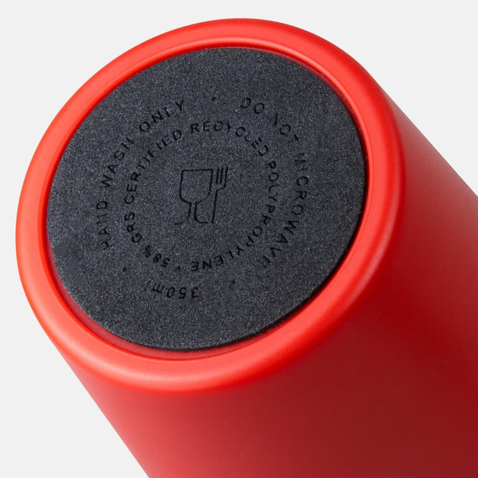 A red coffee cup with a round black base, featuring a logo and instructions for use.