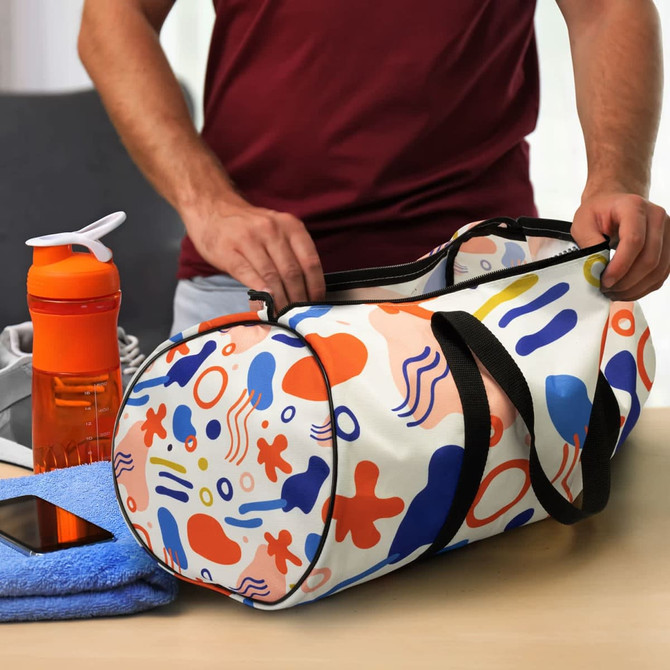 A colourful duffle bag with a vibrant abstract pattern, positioned next to a drink bottle and a towel on a table.