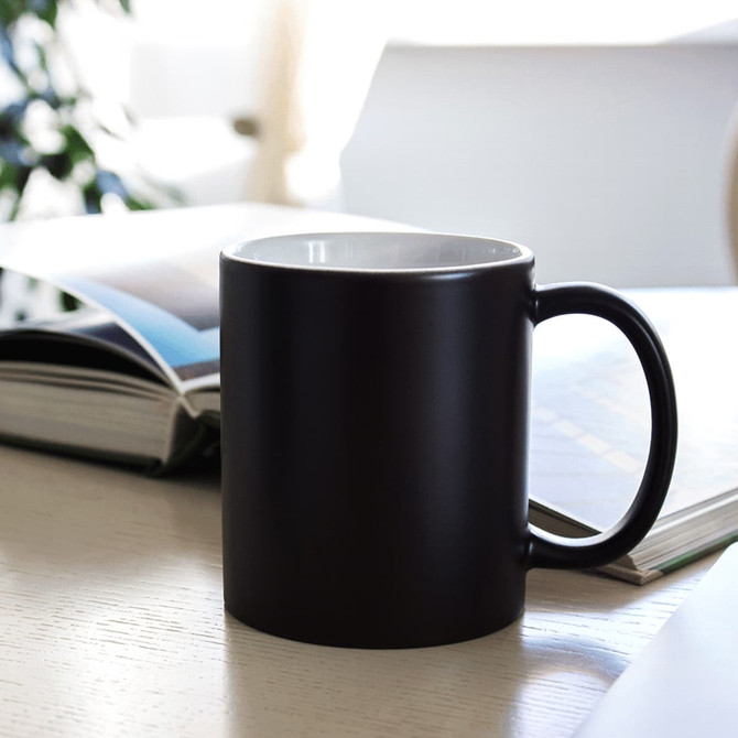 A black ceramic mug with a white interior, placed on a table beside an open magazine.