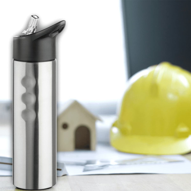 A drink bottle in stainless steel with a black spout and a logo, set against a blurred construction backdrop.