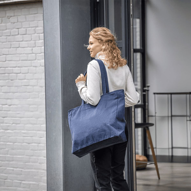 A woman carrying a large navy tote bag with two sturdy handles. The bag appears spacious and made of fabric.