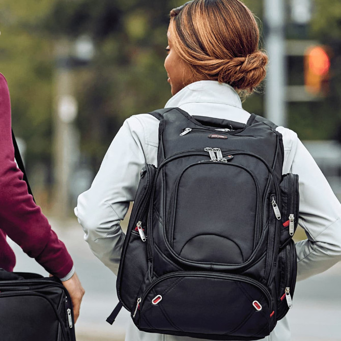 A black backpack with multiple compartments and a logo, carried by a woman outdoors.