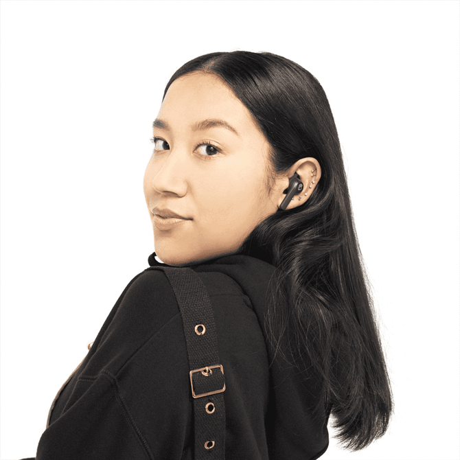 A woman with long, dark hair is wearing black Skullcandy Indy EVO True Wireless earbuds.