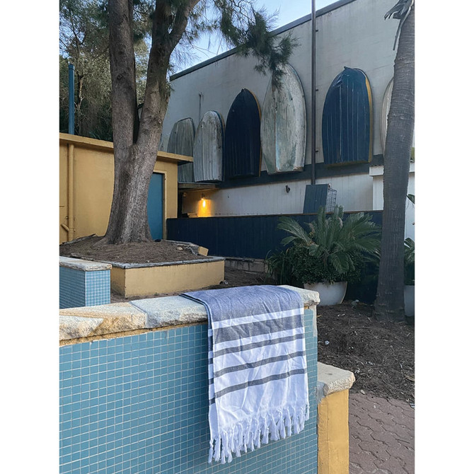 A grey and white striped Turkish beach towel hangs over a stone ledge near a pool, surrounded by trees and buildings.