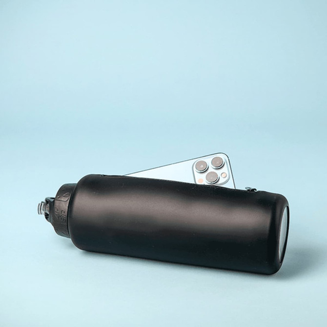 A drink bottle in matte black with a screw cap, featuring a logo and partially hidden behind a smartphone.