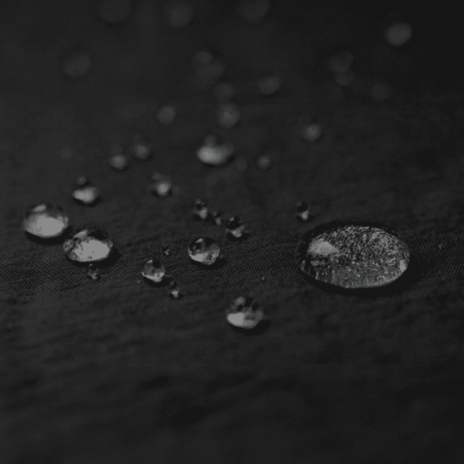 A close-up of water droplets on a textured black surface, showcasing various sizes and reflections.