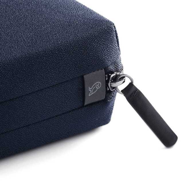 A close-up of a navy blue tech kit with a textured surface and a zip fastening, featuring a small logo.
