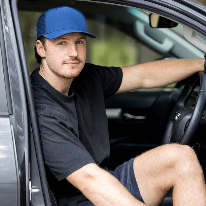 A blue trucker cap with a logo displayed, worn by a person sitting in a car.