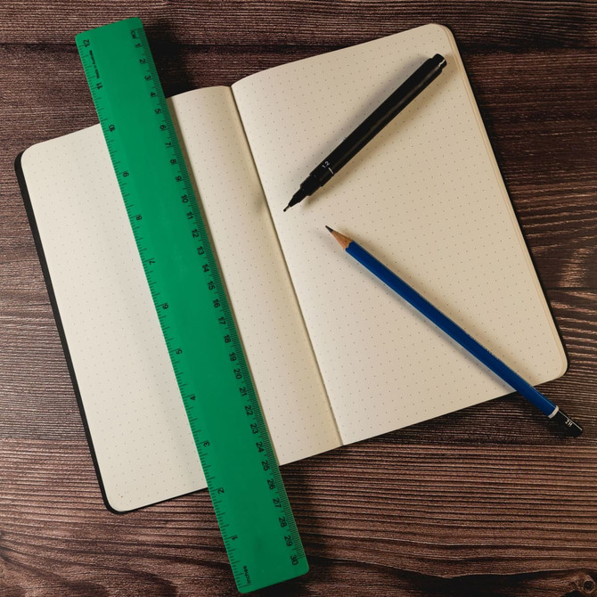 A green 30cm recycled plastic ruler lies on an open notebook with a black pen and blue pencil beside it.