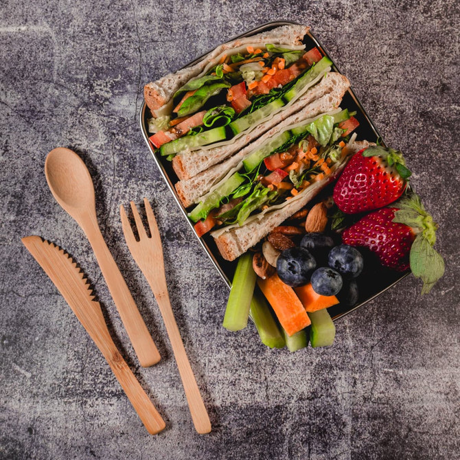 A lunch box contains sandwiches with lettuce, tomato, and carrot, alongside strawberries, blueberries, almonds, celery, and carrot sticks.