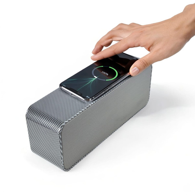 A silver speaker with a textured surface and a smartphone placed on top for charging.