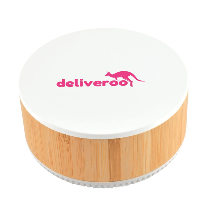A round wireless charger and speaker with a bamboo base and a white top featuring the Deliveroo logo in pink.
