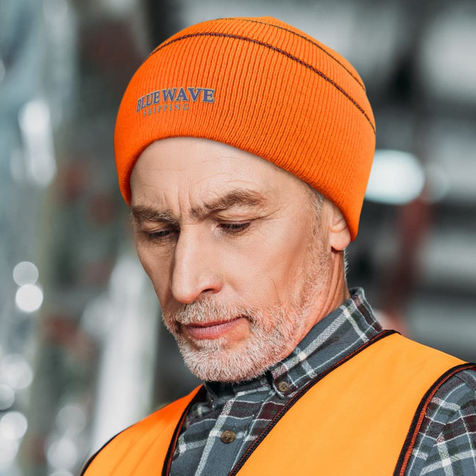 An orange, high-visibility beanie worn by a man, featuring a logo and a close-up view of his expression.