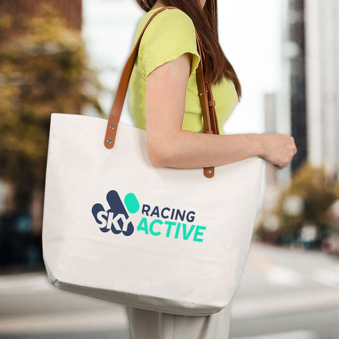 A cream cotton tote bag with brown straps, featuring a logo design on the front.