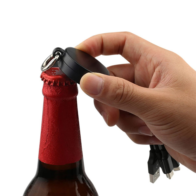 A drink bottle opener with a black circular design and attached charging cables is being used to open a red bottle cap.