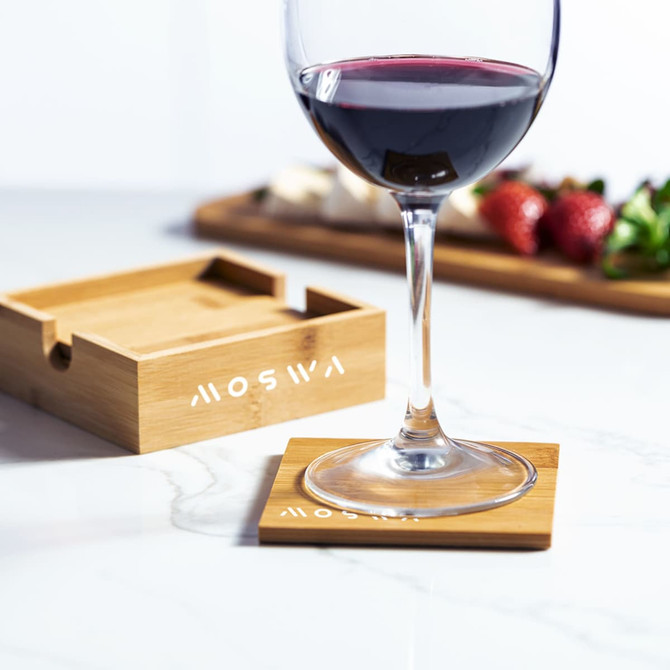 A bamboo coaster sits on a marble surface under a wine glass, alongside a wooden tray with strawberries and salad.