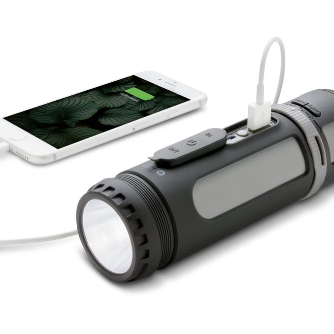 A black multifunctional speaker with a flashlight, connected to a smartphone for charging.