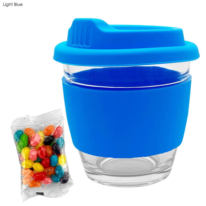A light blue reusable coffee cup with a silicone sleeve and a clear glass body, accompanied by a bag of jelly beans.