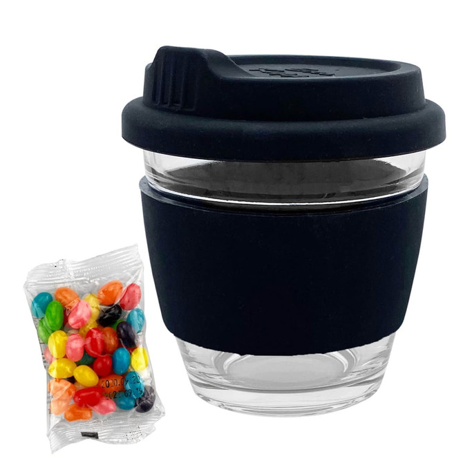 A reusable glass coffee cup with a black silicone sleeve, accompanied by a pack of colourful jelly beans.