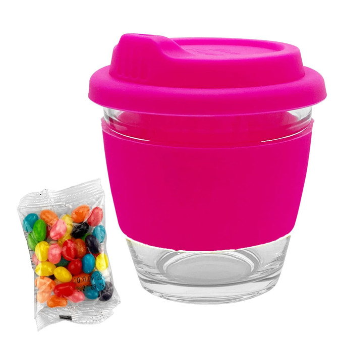 A reusable glass coffee cup with a bright pink silicone sleeve and lid, alongside a pack of colourful jelly beans.