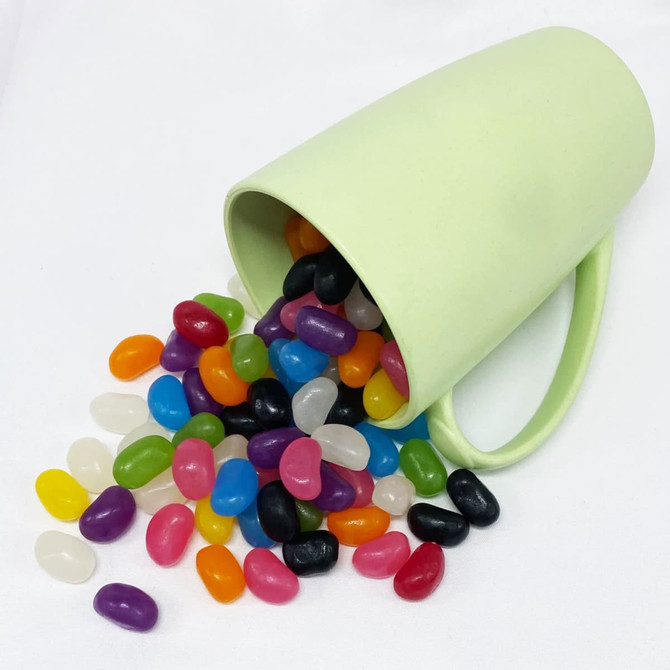 A green bamboo mug tipped over with an assortment of colourful jelly beans spilling out.