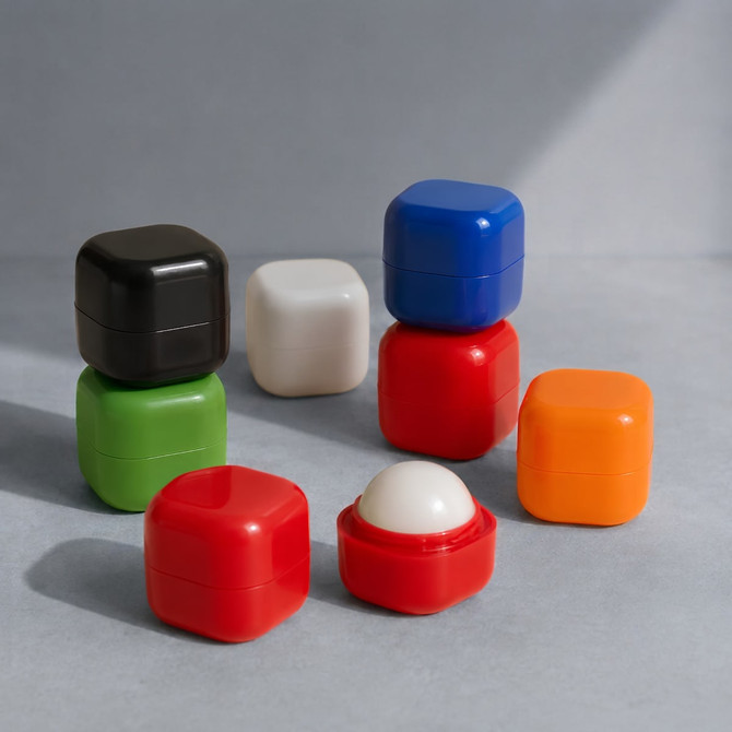 A collection of colourful lip balm cubes in black, white, green, red, blue, and orange, some opened to reveal the balm.