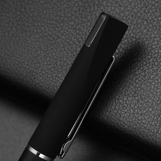 A sleek black metal pen with a silver clip, resting on a textured black surface. The pen features a logo.