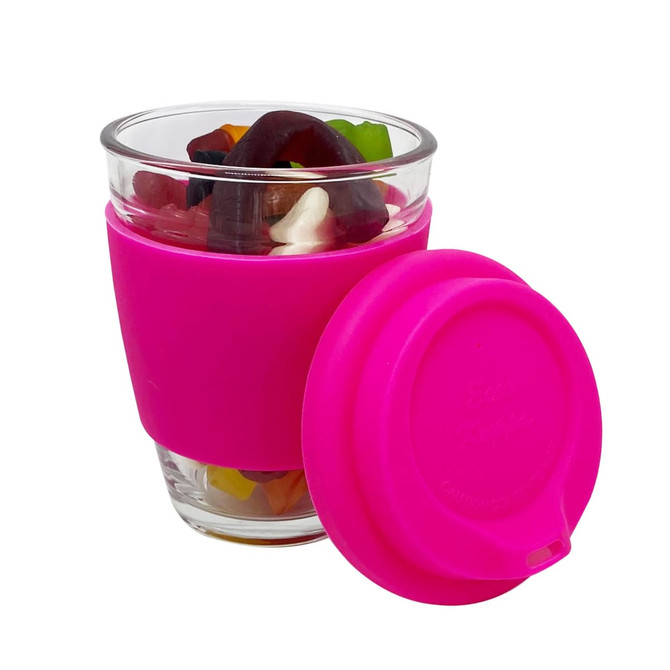A pink silicone sleeve coffee cup with a clear glass body, filled with colourful jelly lollies and a pink lid.