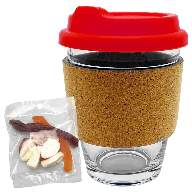 A glass coffee cup with a red lid and cork band, accompanied by a bag of mixed coloured lollies.
