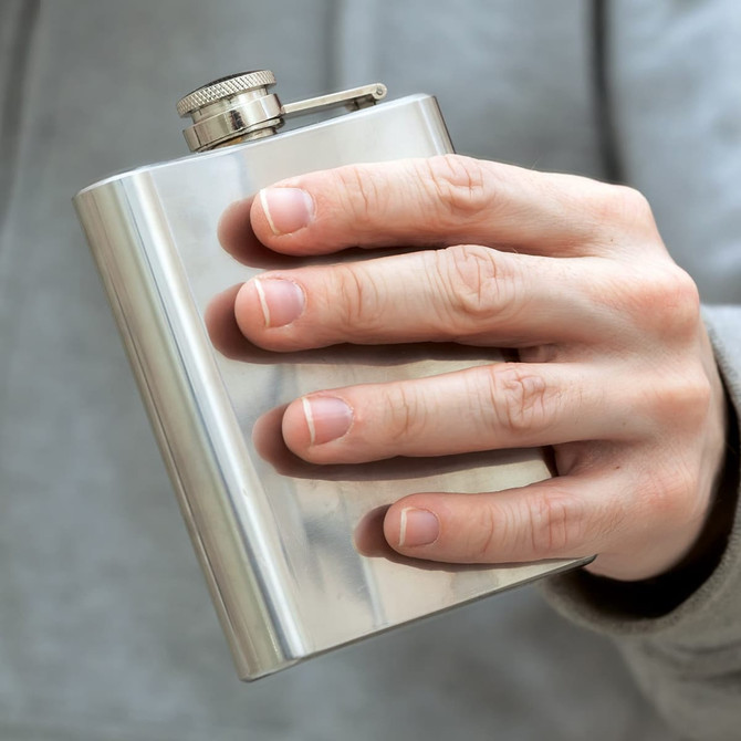 A stainless steel hip flask held in a hand, featuring a screw-top lid and a logo on the front.