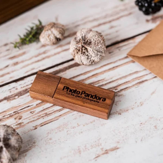 A wooden USB flash drive with a dark brown finish, featuring a logo, placed on a rustic wooden surface.