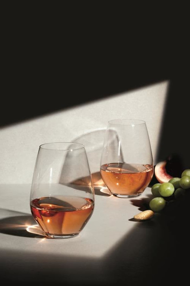 Two clear stemless wine glasses filled with rosé wine, accompanied by grapes and almonds on a light surface.