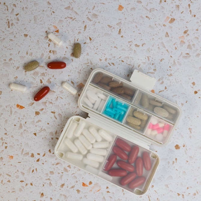 A compact white pill organizer with multiple compartments filled with various colored pills scattered around.