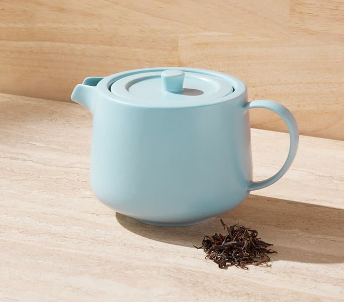 A light blue teapot with a lid and handle, accompanied by loose tea leaves. The teapot includes an infuser.
