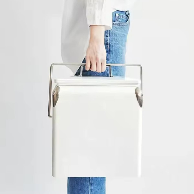 A white metal ice cooler box with a silver handle being held by a person in blue jeans. It features a logo.