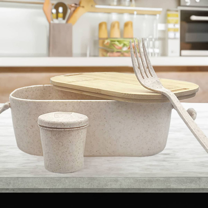 A bamboo lunch box with a light pink hue, accompanied by a small container and a fork, set on a kitchen countertop.