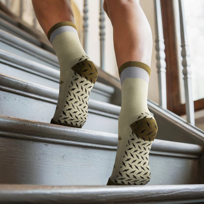 Grip socks in green and grey with a patterned sole, featured on a person ascending wooden stairs.