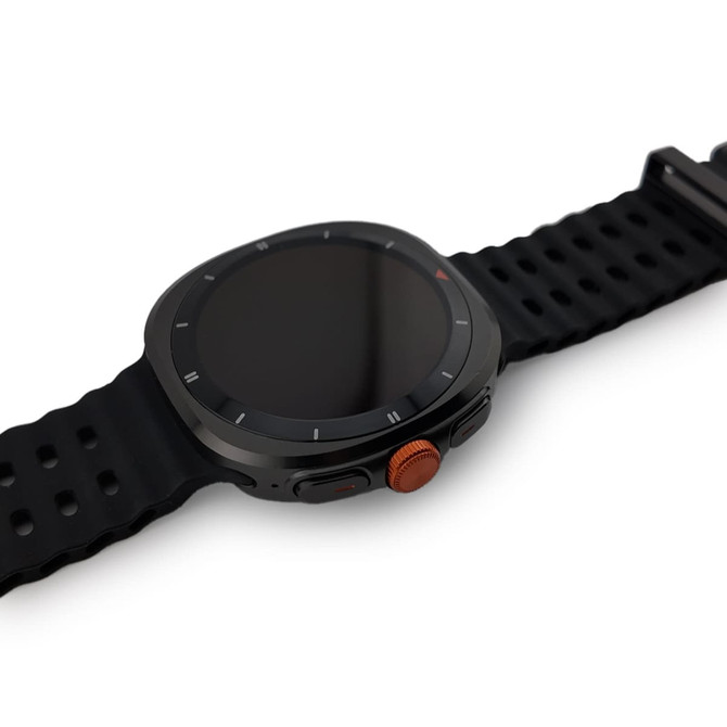 A black smart watch with a round face and a textured orange button on the side. The strap is made of a flexible material.