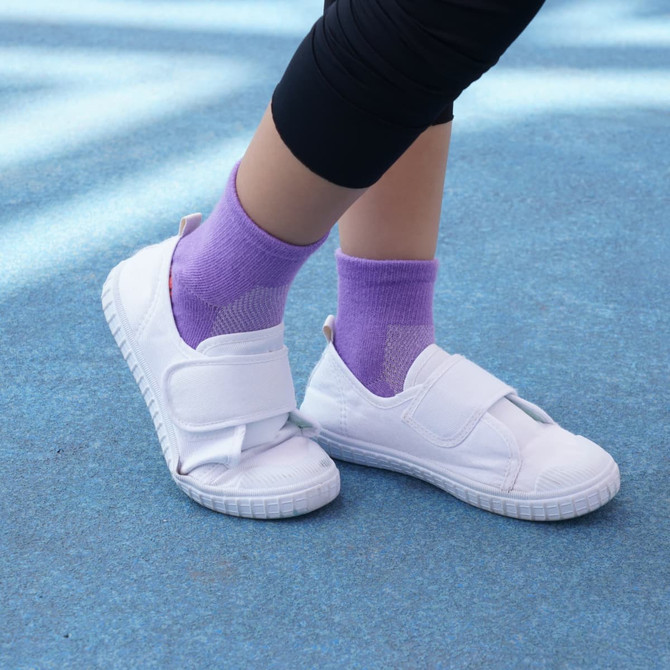 Purple crew socks worn with white shoes on a blue surface. The socks have a textured design.