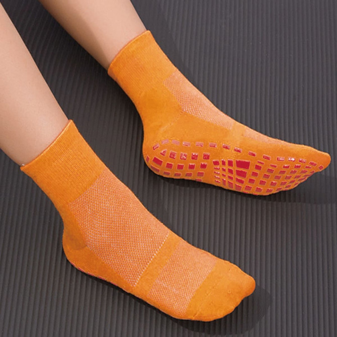 Bright orange gripper socks featuring textured soles and ankle height, designed for improved traction and comfort.