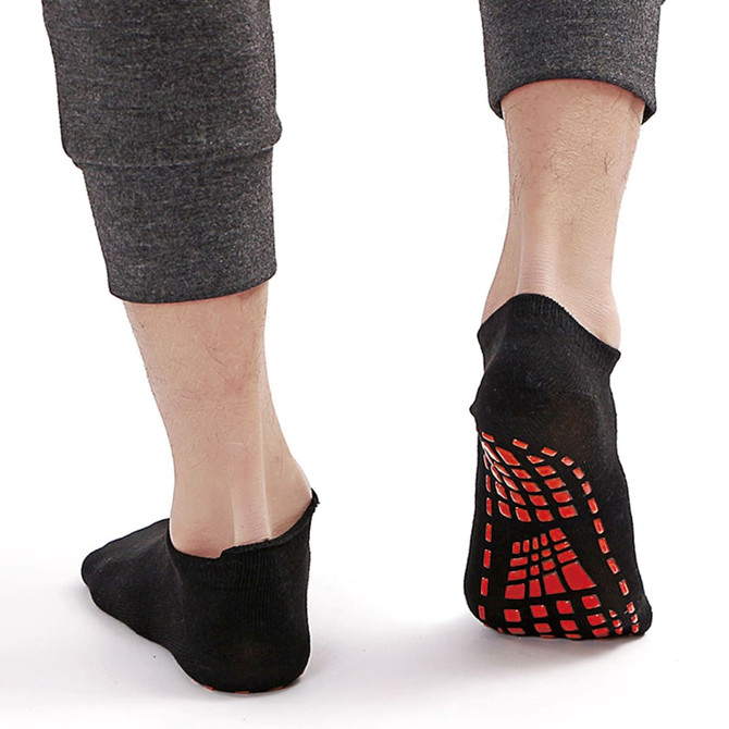 Low cut black kids' gripper socks with a red traction pattern on the sole, displayed on a person's feet.